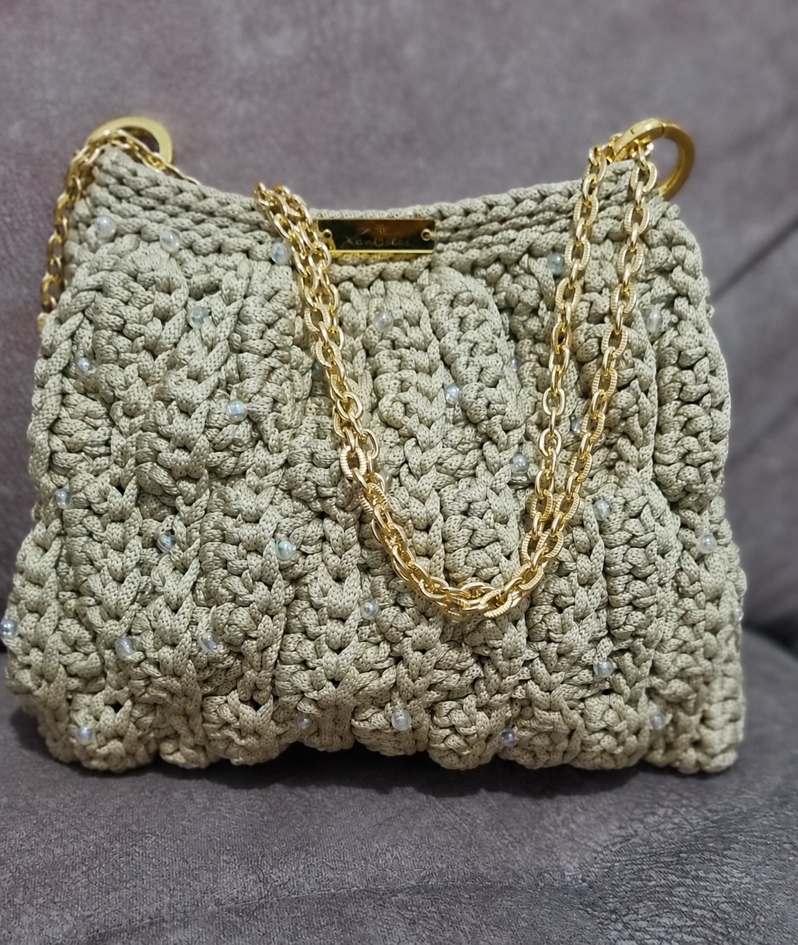 Foto caseira de uma bolsa de crochê com corrente dourada sobre o sofá