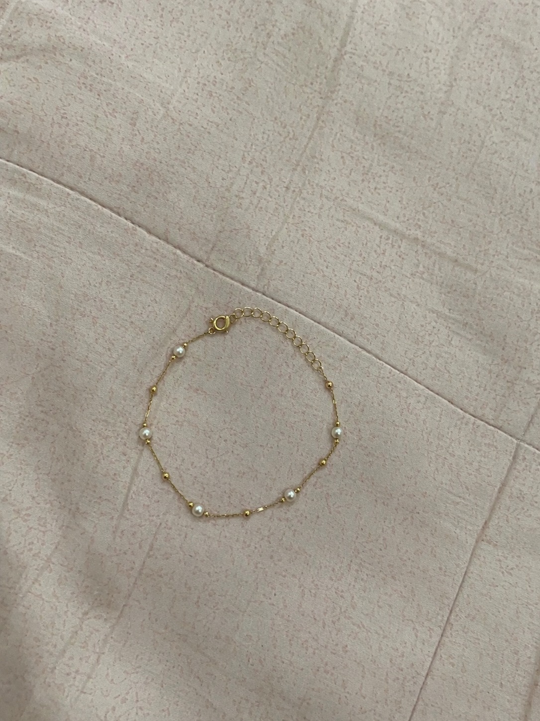 Foto amadora de uma pulseira dourada com pérolas sobre a mesa